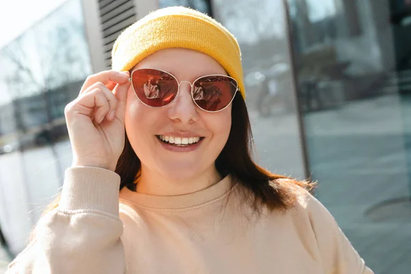 Szczęśliwa, wesoła młoda kobieta spacerująca ulicą miasta. Portret pięknej kobiety w żółtym kapeluszu i różowych okularach słonecznych uśmiechniętych na zewnątrz. Koncepcja miejskiego stylu życia. Podróżnik — Zdjęcie stockowe