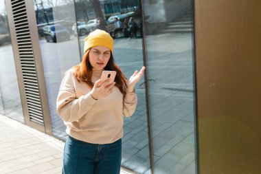 Yakından bakınca üzgün, şüpheci, mutsuz, ciddi bir kadın açık havada telefon ekranına bakıyor. Negatif insani duygu yüz ifadesi hissi, yaşam reaksiyonu. Kötü haber.