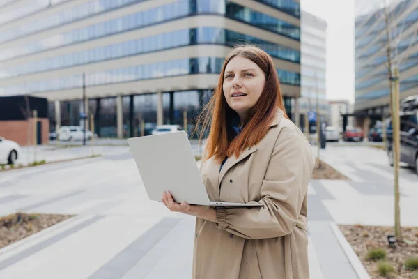 Moda ofis kıyafetleri içinde beyaz bir iş kadını dışarıda dizüstü bilgisayarla poz veriyor. Dizüstü bilgisayarda başarılı bir kadın. Açık ofis. İş konsepti..