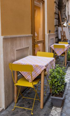 Empty tables and yellow chairs by a trattoria in Rome, Italy. Cozy old street, Outdoor eating concept, traveling