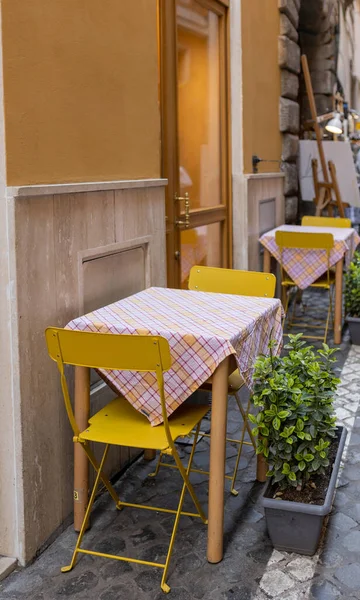 Mesas vacías y sillas amarillas junto a una trattoria en Roma, Italia. Acogedora calle vieja, concepto de comer al aire libre, viajar — Foto de Stock