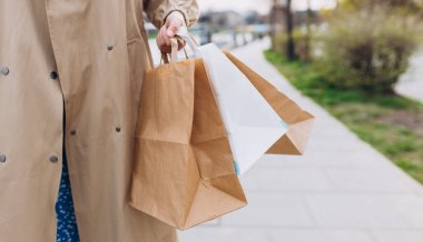Cropped view of woman in autumn wear holding shopping paper bags in hands, walking at street, black friday. Urban lifestyle concept. Delivery carrying.