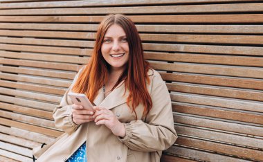 Mutlu, genç bir kadın bankta oturuyor ve şehir caddesinde akıllı telefon kullanıyor. Şehir yaşam tarzı konsepti. Gezgin, Online alışveriş, uygulama kullanarak