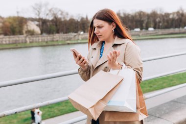 Telefonu kullanan ve kötü haberler okuyan üzgün genç bir kadın. Şehir caddesinde yürüyen üzgün düşünceli bir kız. Negatif insanların duyguları. Kızıl saçlı kız elinde kağıt alışveriş torbaları tutuyor, özel bir teklif yok, satışlar bitti.