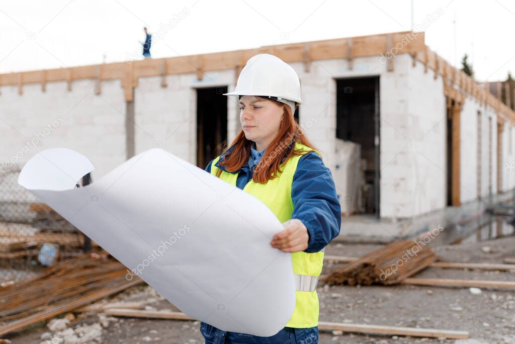Architect with a blueprints at a construction site. Portrait of successful woman constructor wearing white helmet and safety yellow vest. Woman are planning new project.