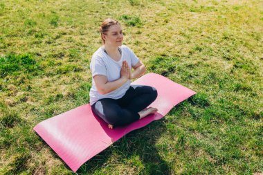 Genç gülümseyen kızıl saçlı kadın yoga yapıyor Ardha Padmasana egzersizi yapıyor ve yarım Lotus 'ta meditasyon yapıyor.