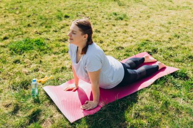 Kobra pozu veren bir kız, tam boy. Doğada yoga yapan genç bir kadının portresi. Rahatlamak ve yoga yapmak. Sağlık ve sağlıklı bir yaşam tarzı. Bhujangasana