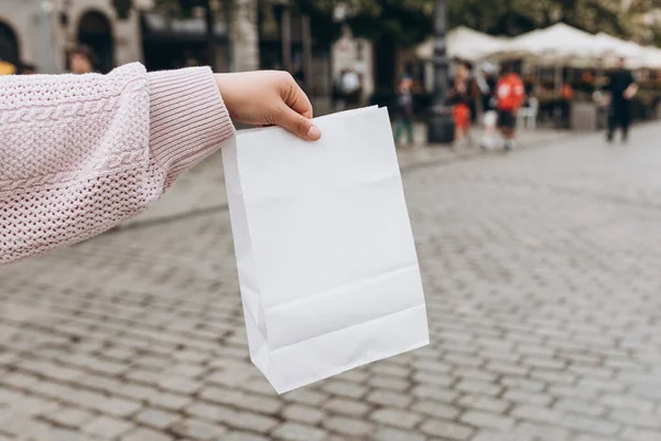 Kadın, arka planda paket almak için beyaz, boş, boş bir kese kağıdını elinde tutuyor. Paketleme şablonu maketi. Teslimat hizmeti kavramı.