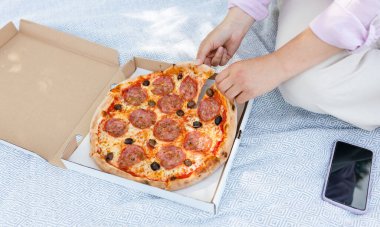 Doğada piknikte otururken lezzetli biberli pizza yiyen bir kız..