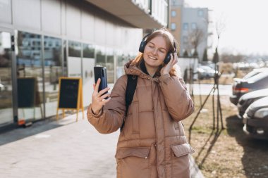 Şehirde sokakta yürüyen mutlu genç bir kadının portresi. Dışarıdaki telefon ve kulaklıkla görüntülü konuşma yapan bir kız, blog yazarı hikayeleri kaydediyor.