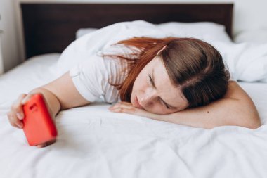 Bir battaniyenin altında uyuyan genç bir kadın uyanıyor ve akıllı telefonunu kontrol ediyor. Kız Alarm N Cep Telefonunu Kapatıyor