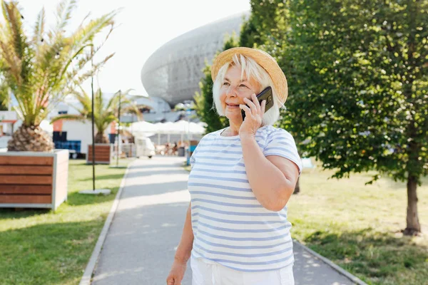 Beautiful Mature woman in trendy wear spending time on street using smartphone. Happy senior talking on the mobile phone, warm sunny day. Urban concept, technology banner