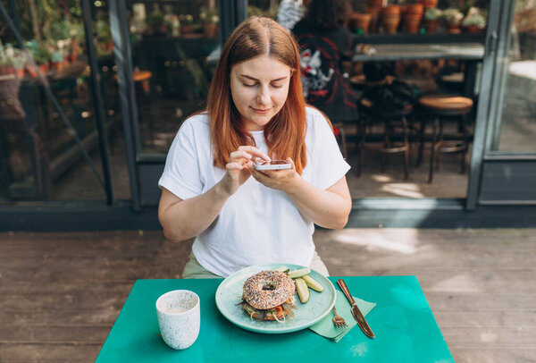 Young woman sitting in the restaurant and taking pictures of the food with mobile phone