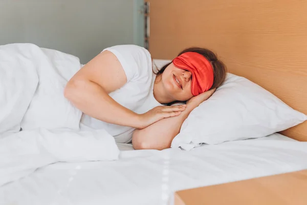 Young beautiful woman sleeping in bed with pink eye mask. Caucasian girl sleeping on soft pillow, enjoying sweet dreams good night rest in bed.