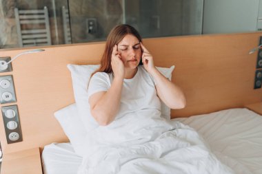 Young Woman with hard headache holding hand on head. Covid-19 new variant - Omicron. Pandemic infection. Upset woman lying in bed feel sick or distressed