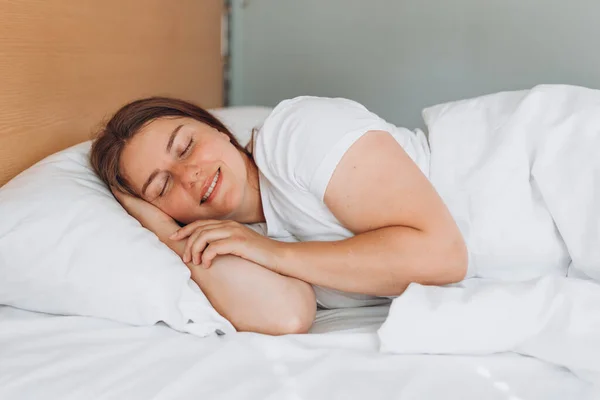 Young beautiful woman sleeping in bed at home. Millennial Caucasian girl sleeping on soft pillow, enjoying sweet dreams good night rest in bed.