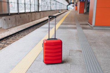 Forgotten travel bag on the train station. Red suitcase on empty station platform. Travel and vacation theme background.