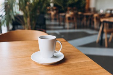 A Cup of freshly brewed black tea at a cafe blurred background. Coffee cup on table cafe shop Interior. Concept of easy breakfast. One white big ceramic cup. Top view.