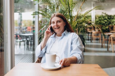 Telefonla konuşan, yağmurlu bir günde evde çay ya da kahve içen bir kadın. Genç ve neşeli bir bayan komik bir konuşma sırasında eğleniyor..