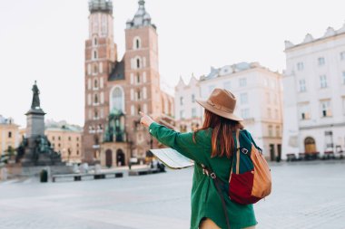 Çekici bayan turist yeni şehri keşfediyor. Kızıl saçlı kadın Krakow 'daki Pazar Meydanı' nda bir harita tutuyor. Sonbaharda Avrupa 'yı geziyorum. Aziz Mary Bazilikası