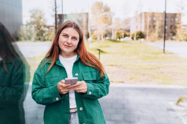 Genç mutlu iş kadını şehirde gülümsüyor ve akıllı telefon kullanıyor. Ofise giden güzel bir kadın akıllı telefonuyla internetten bilgi arıyor. İş, eğitim kavramı