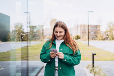 Genç mutlu iş kadını şehirde gülümsüyor ve akıllı telefon kullanıyor. Ofise giden güzel bir kadın akıllı telefonuyla internetten bilgi arıyor. İş, eğitim kavramı