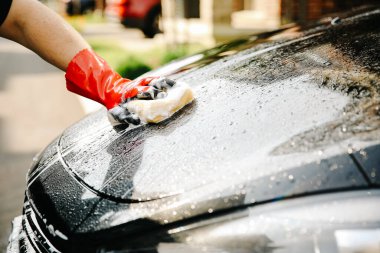 Kırmızı eldivenli bir erkek siyah arabayı yıkamak için sünger tutuyor..