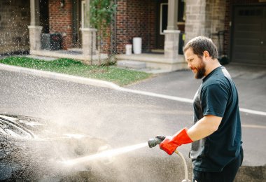 Kakuasyalı bir adam evinin önünde su jeti ile araba yıkıyor..
