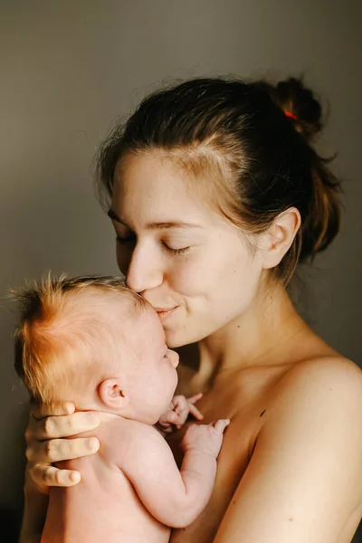 Porträtt av mor som håller och kysser nyfödda barn. Royaltyfria Stockbilder