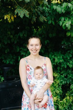 Parkta bebeği tutan beyaz bir kadının portresi..