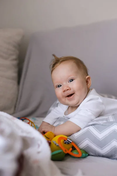 Newborn adorable baby lying on grey bedspread and playing with toys. — Stock Photo, Image