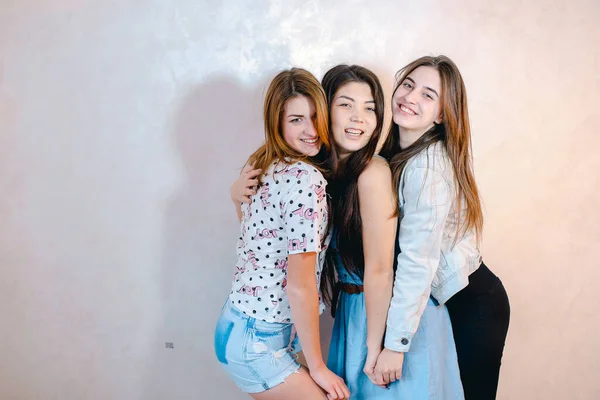 Grappige meisjes poseren in camera met een glimlach op hun gezicht en staan tegen de achtergrond van licht muur in de kamer. — Stockfoto