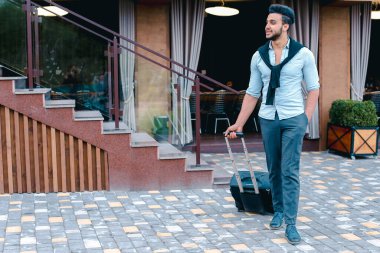 Genç adam Arap işadamı öğrenci geldiysen oraya restoran ile bavul için elinde, kamera, durur ve uzak görünüyor gülümseyen.