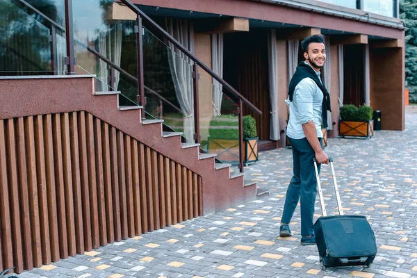 Joven chico árabe empresario estudiante vino a restaurante con maleta en la mano, sonriendo a la cámara, se detiene y mira hacia otro lado . — Foto de Stock