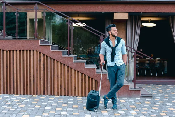 Joven chico árabe empresario estudiante vino a restaurante con maleta en la mano, sonriendo a la cámara, se detiene y mira hacia otro lado . — Foto de Stock
