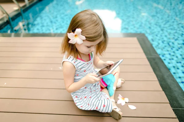 Pequeña linda chica utiliza la tableta en la piscina de fondo, wearin — Foto de Stock