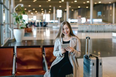 Havaalanı hall yanında valiz tablet ile internet kullanan kadın.