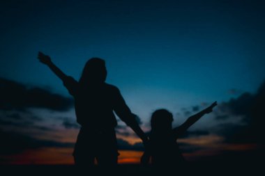 Siyah silhouette kadın ve küçük kız vening, gün batımı arka plan yürüyüş.