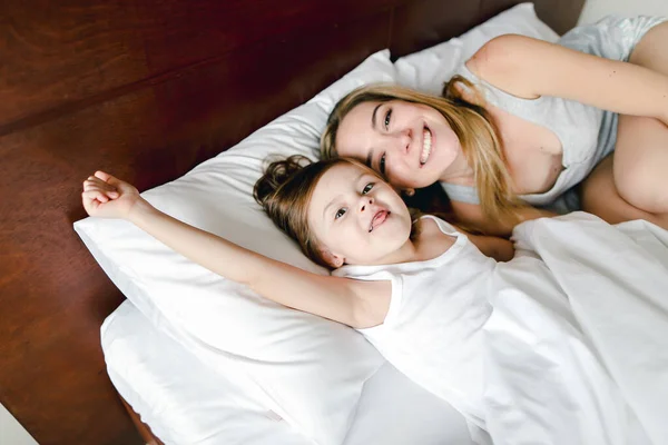 Mãe feliz deitada na cama com a pequena filha jocund . — Fotografia de Stock