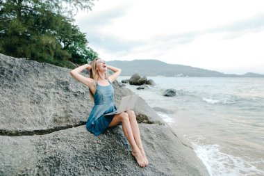 Deniz kıyısında laptop ile çalışma ve taş üzerine oturan genç kız.