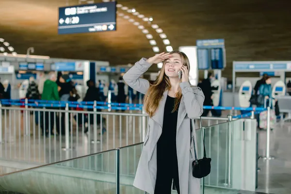 Dziewczyna rozmawia przez smartfona i szuka przyjaciela na lotniska. — Zdjęcie stockowe