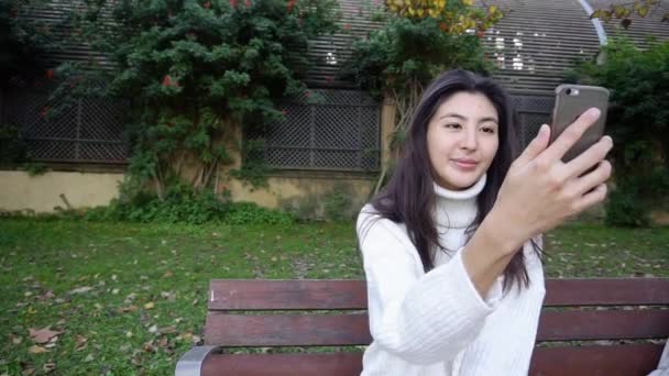 Slow Motion chica japonesa sentada en el banco y haciendo videollamada por teléfono inteligente. — Vídeo de stock
