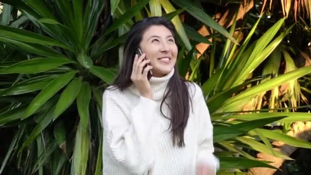 Молодая женщина пользуется телефоном в наушниках во время прогулки — стоковое видео