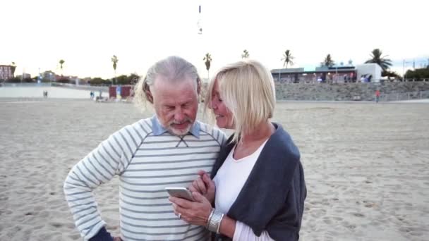Szczęśliwy starszy mężczyzna i kobieta kilka siedzieli przy stole przy plaży rozmowy na telefon komórkowy — Wideo stockowe
