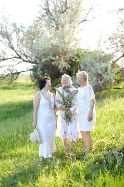 Mutlu kızlar dışarıda yaşlı anneleriyle dikiliyor ve beyaz elbiseler giyiyor..