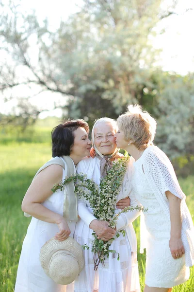 Two happy daughters kissing old mother outside and wearing white dresses. — Stock Photo, Image