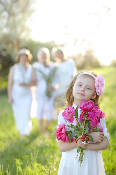 Menina em vestido branco mantendo flores, família embaçada no fundo. — Fotografia de Stock