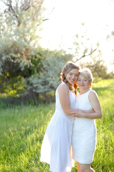 Caucasian girl hugging mother outside and wearing white dress. — Stock Photo, Image