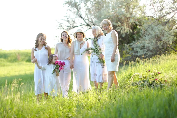 Glad mormor stående med döttrar och barnbarn, klädd i vita kläder utanför. Stockfoto