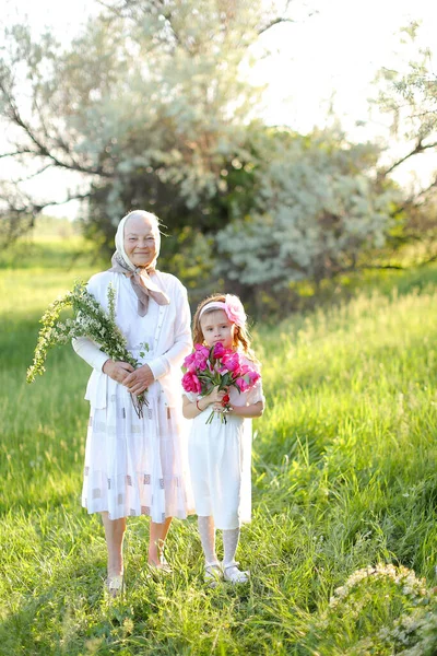 Stara babcia stojąca z małą wnuczką i trzymająca kwiaty. — Zdjęcie stockowe